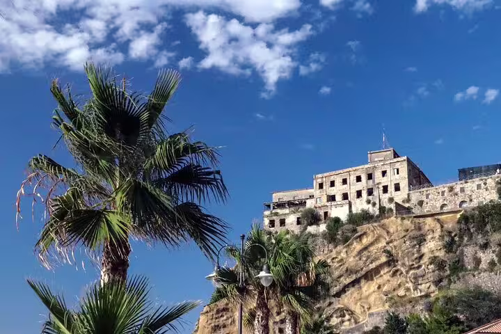 Historic clifftop building and palm trees under blue skies in Pizzo Calabro, seen on a private guided walking tour in Calabria
