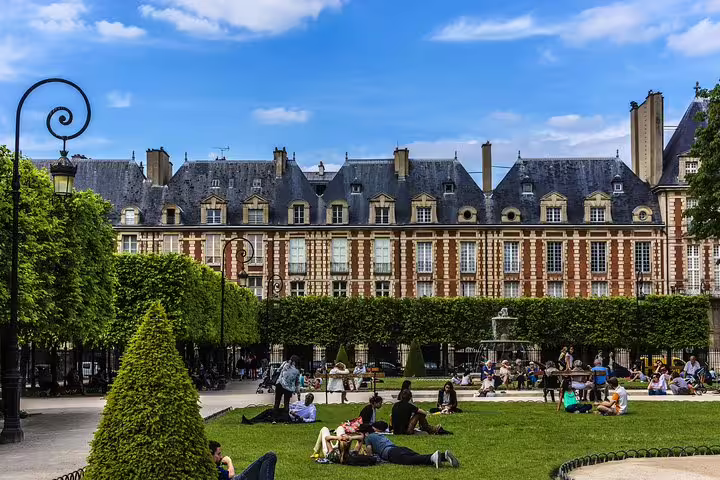 People relax on the grass in the picturesque Place des Vosges, Paris, surrounded by historic architecture and lush greenery.