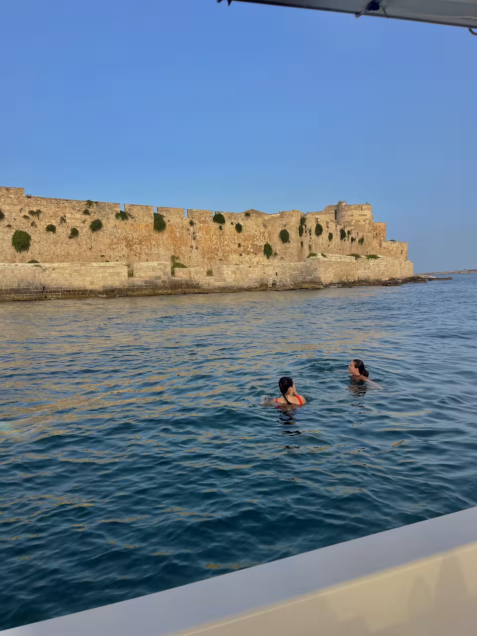 Swimmers enjoying the sea near historic fortifications at Plemmirio, perfect for a cultural and aquatic tour.