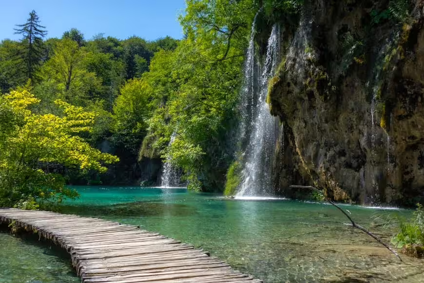 Scenic Plitvice Lakes boardwalk beside clear lagoon and cliff waterfall, Croatia guided group tour experience
