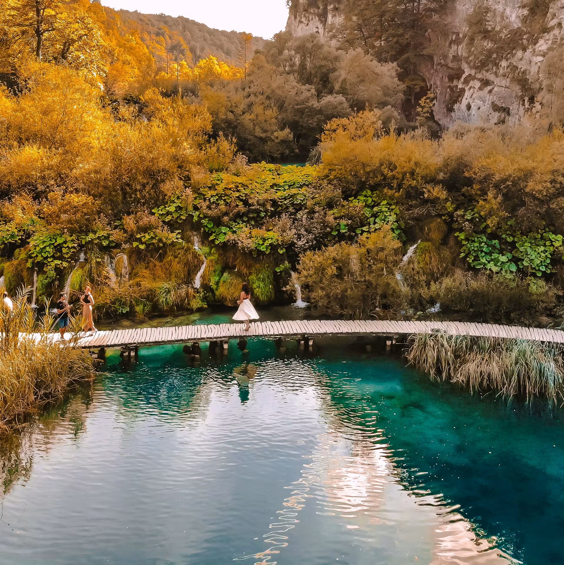 Visitors crossing Plitvice Lakes boardwalk above crystal-clear water and cascades, guided day trip from Zadar