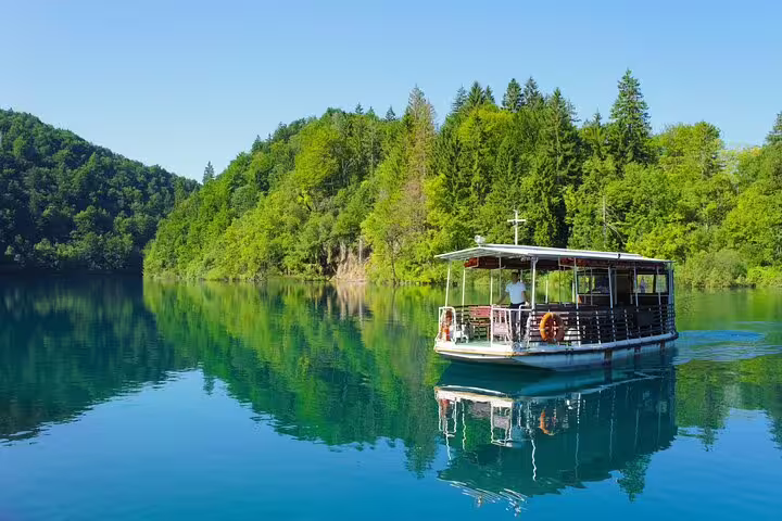 Electric boat cruising a calm Plitvice lake with forest reflections, scenic stop on private tour from Split