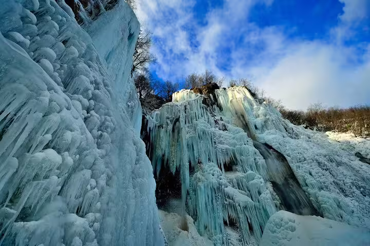 Close-up of frozen Plitvice Lakes waterfall with blue ice formations under clear sky, Croatia admission ticket