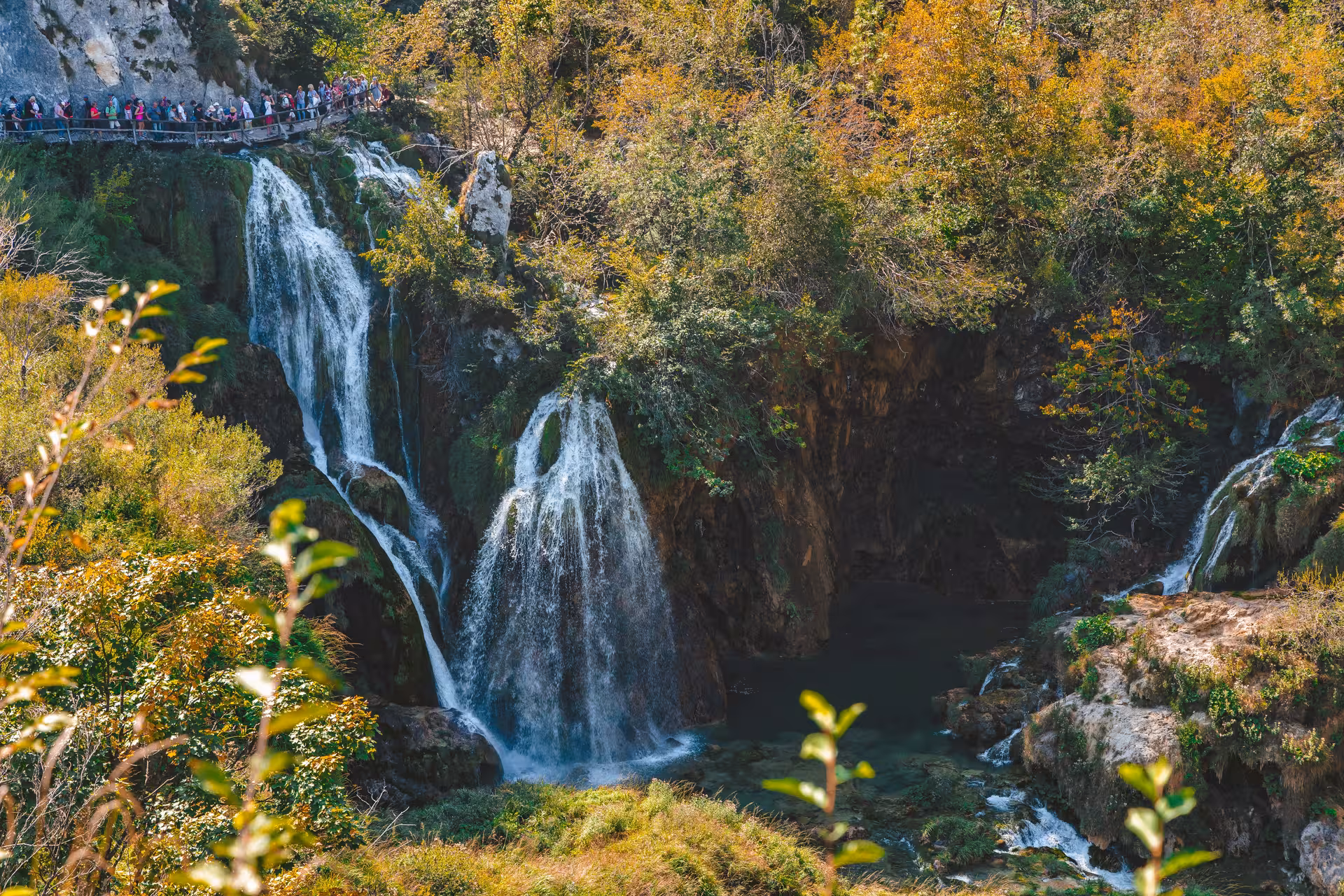 Crowds on boardwalk by cascading Plitvice Lakes waterfalls in autumn, National Park day tour from Zadar