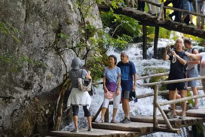 Visitors walking wooden boardwalk beside waterfalls in Plitvice Lakes National Park on Zagreb private tour
