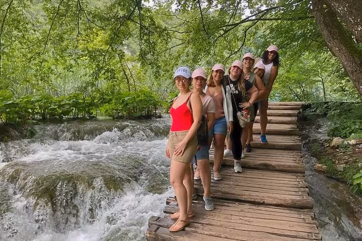 Friends on wooden boardwalk beside rushing falls in Plitvice Lakes on private day trip from Zagreb