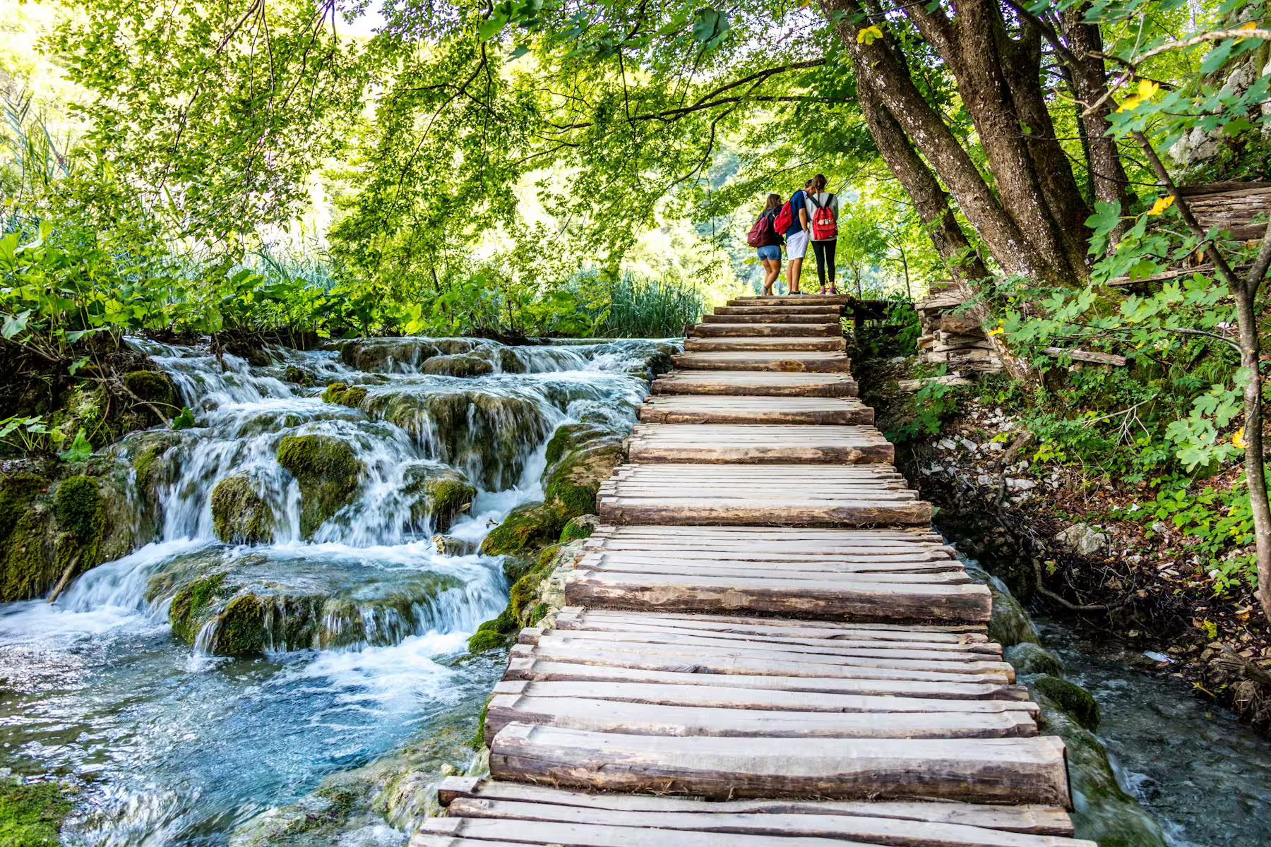 Hikers on Plitvice Lakes wooden trail beside cascades, guided day tour from Zadar and Biograd, Croatia