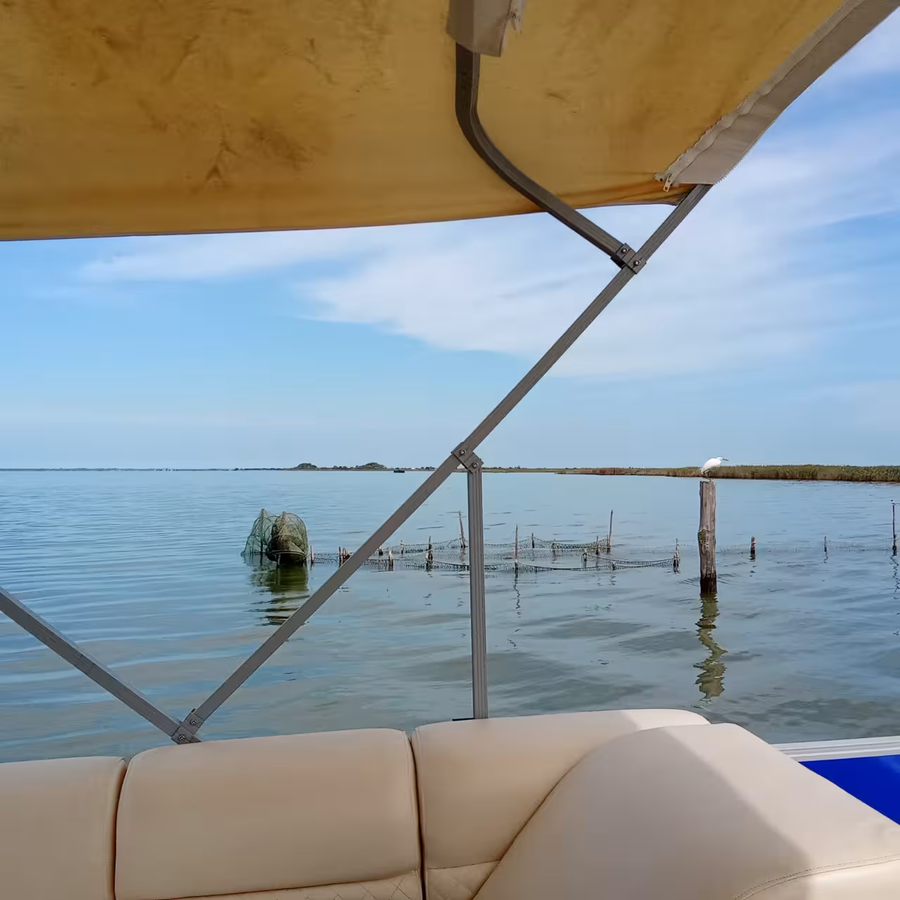 View from covered boat across calm Po Delta lagoon, wetlands and fishing nets on Isola dell’Amore aperitif cruise