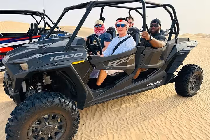 Group riding Polaris RZR 1000 dune buggy across golden desert dunes on an off-road quad bike tour