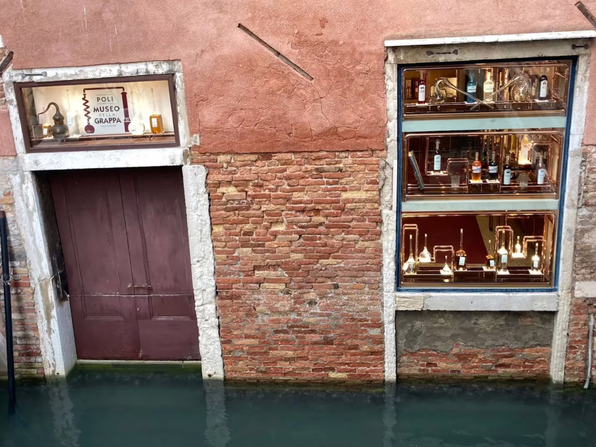 Exterior view of Poli Grappa Museum in Venice, featuring picturesque canal-side brick walls and elegant window displays.