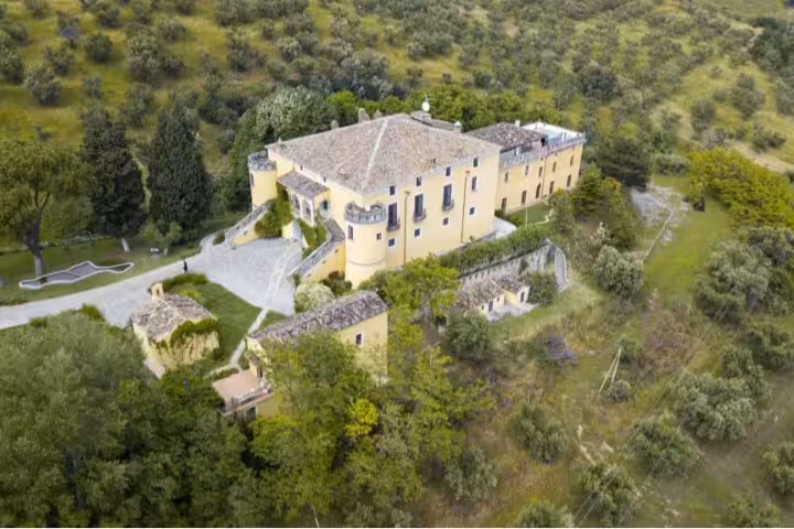 Aerial view of a historic yellow castle retreat in Pollino National Park, surrounded by olive groves and lush hills for yoga escapes