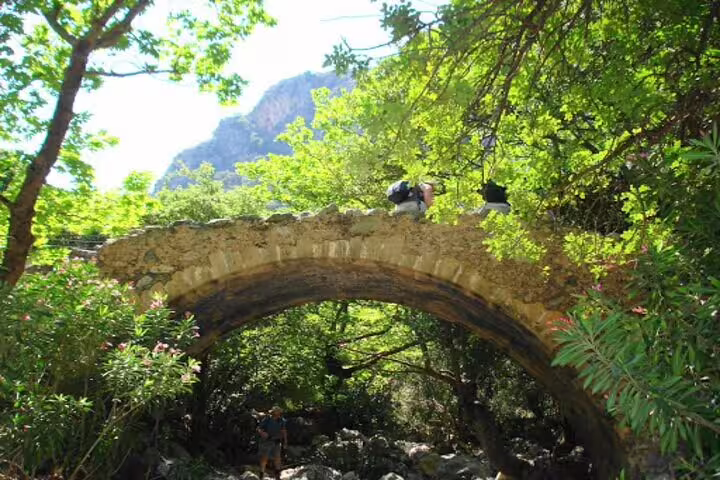 Ancient stone bridge surrounded by vibrant foliage in Polyrrinia, a highlight of the private hiking tour.