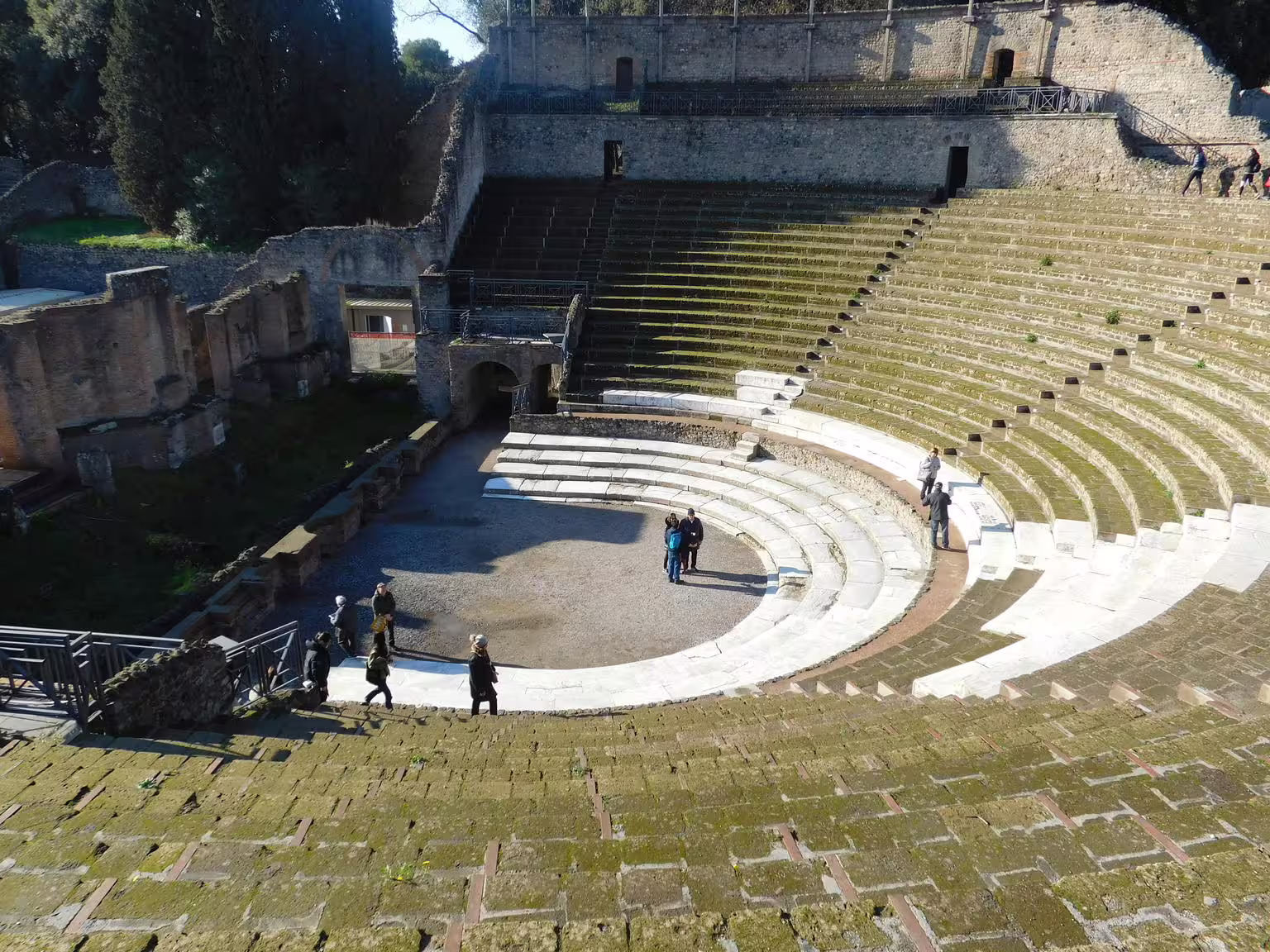 Pompeii amphitheater interior on Naples group tour, Roman seating tiers and visitors exploring ruins