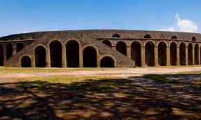 Ancient stone amphitheatre arches in Pompeii under clear blue skies, featured on a guided daily tour from Naples