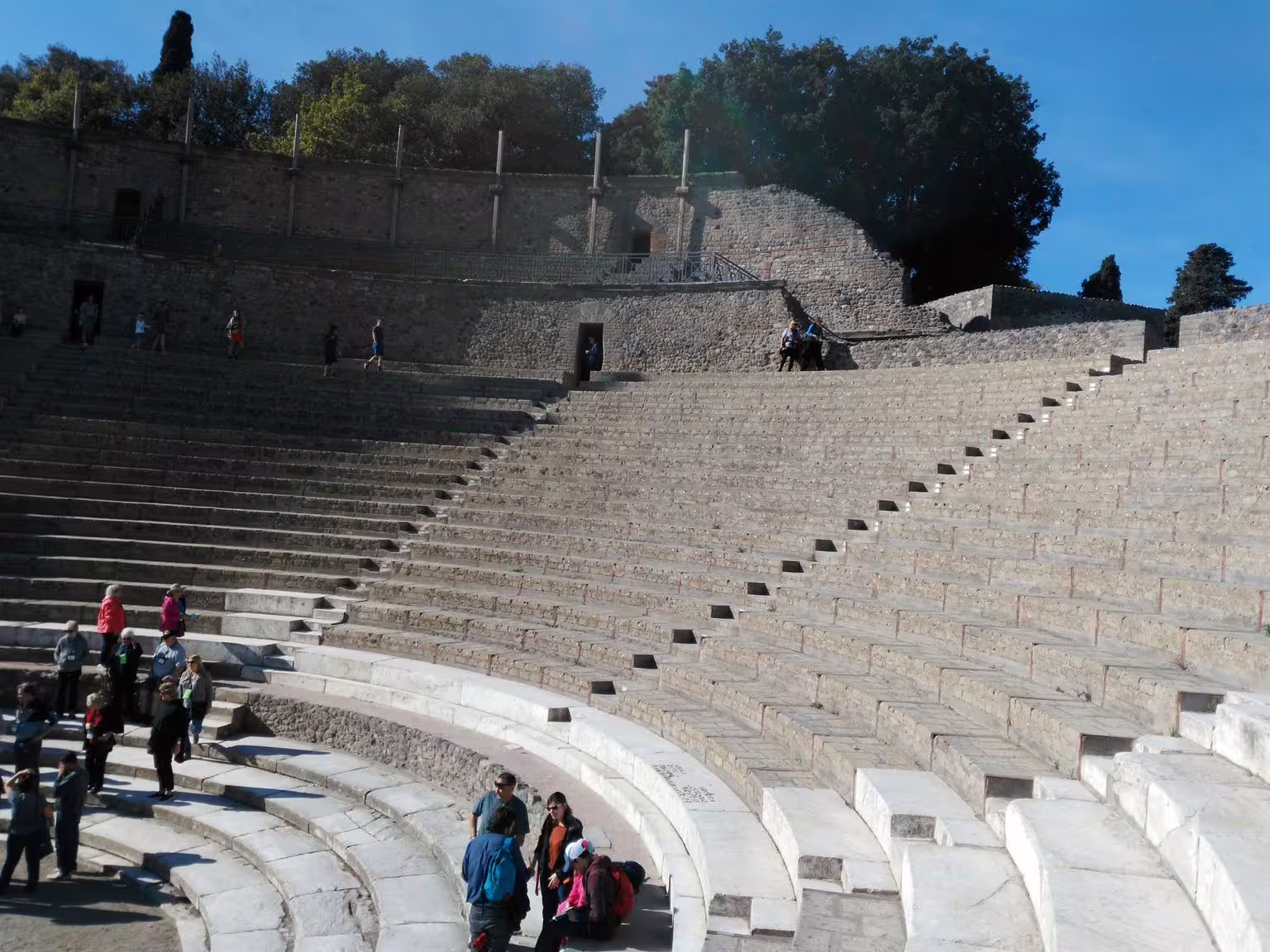 Pompeii amphitheatre seating on Naples group tour, visitors exploring the ancient Roman arena in bright sunlight