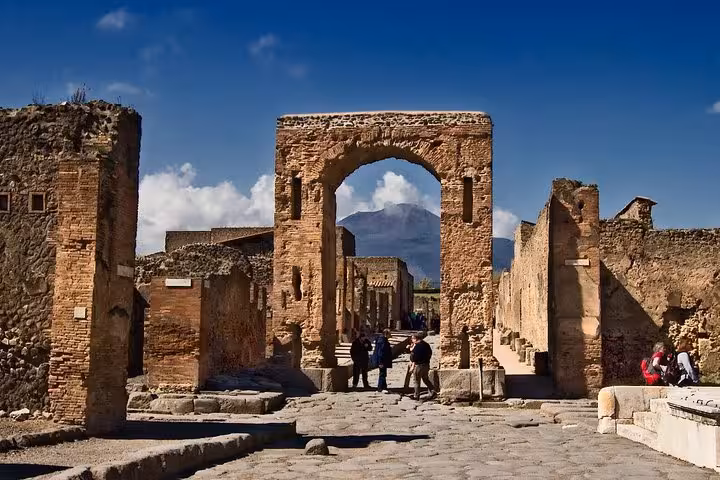 Visitors exploring the ancient archway leading to Pompeii's ruins with Mount Vesuvius in the background.