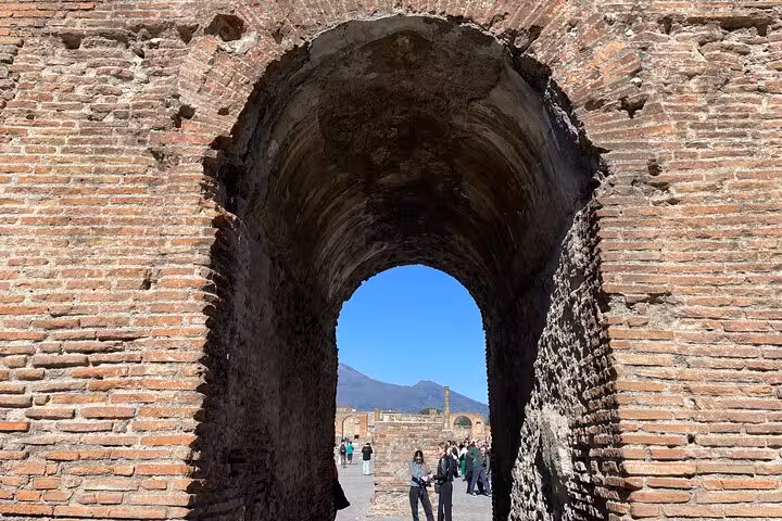 Explore ancient brick archways in Pompeii with Mount Vesuvius in the background on a guided day trip from Rome.