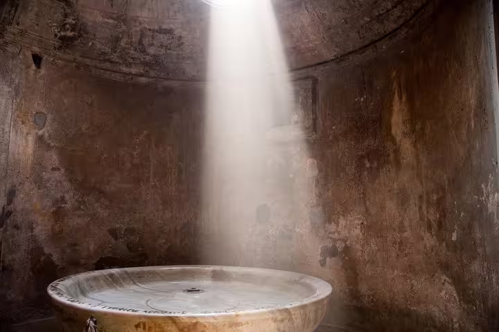 Discover Pompeii's ancient bathhouse with its captivating dome and sunlight streaming onto the central basin.