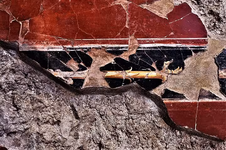 Ancient fresco detail from Pompeii ruins showcasing vibrant red and black hues, featured in guided tour from Positano.