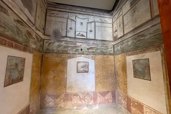 Explore ancient frescoes in a preserved room at Pompeii, showcasing rich Roman art on the Amalfi Coast tour.
