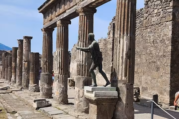 Ancient ruins of Pompeii with a bronze statue and stone columns under a clear blue sky, ideal for a historical day trip.