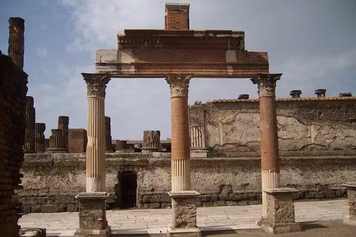 Ancient Pompeii ruins with columns under a cloudy sky, part of guided tour from Sorrento with included lunch.