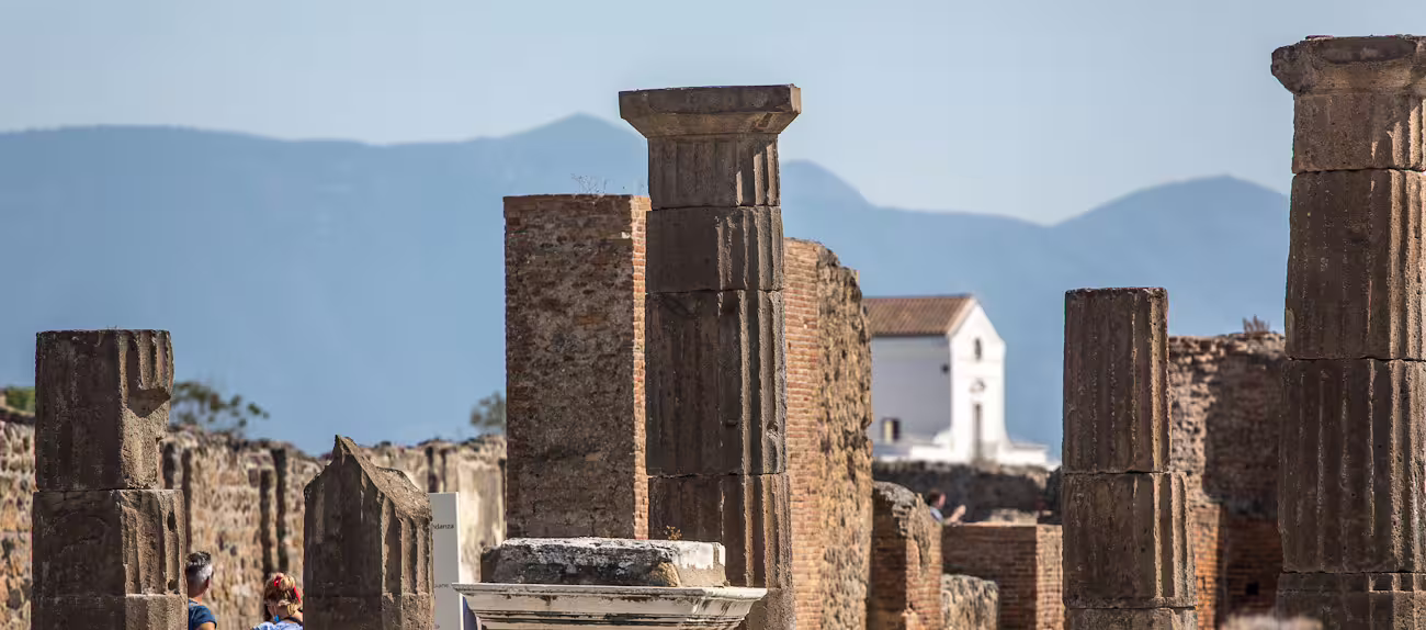 Discover the grandeur of Pompeii's ancient ruins with towering columns set against a picturesque mountain backdrop.