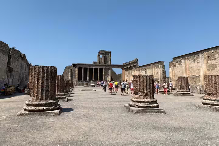 Tourists explore ancient ruins with columns in Pompeii on a guided tour from Sorrento under a clear blue sky.