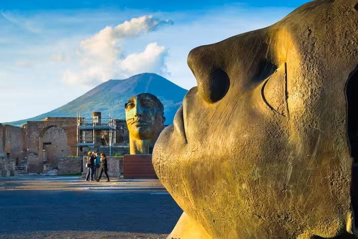 Discover Pompeii's ancient ruins with striking sculptures and Mount Vesuvius in the backdrop on a Sorrento tour.