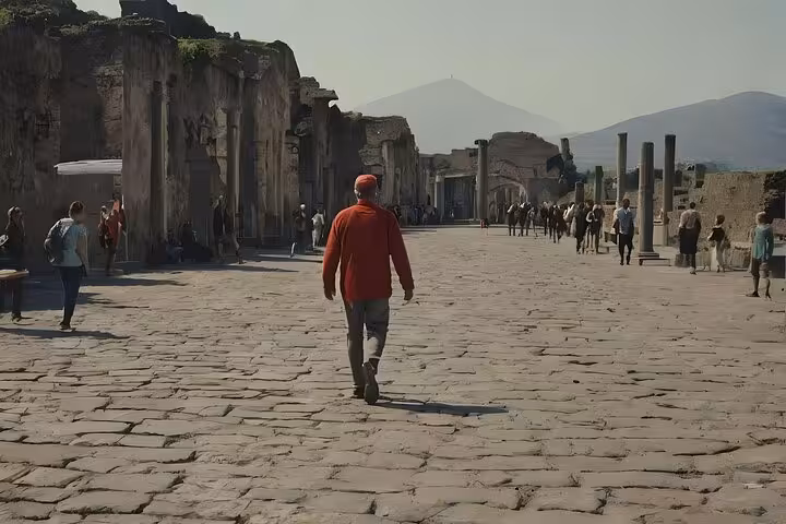 Tourists explore the ancient ruins of Pompeii with Mount Vesuvius in the background on a sunny day.