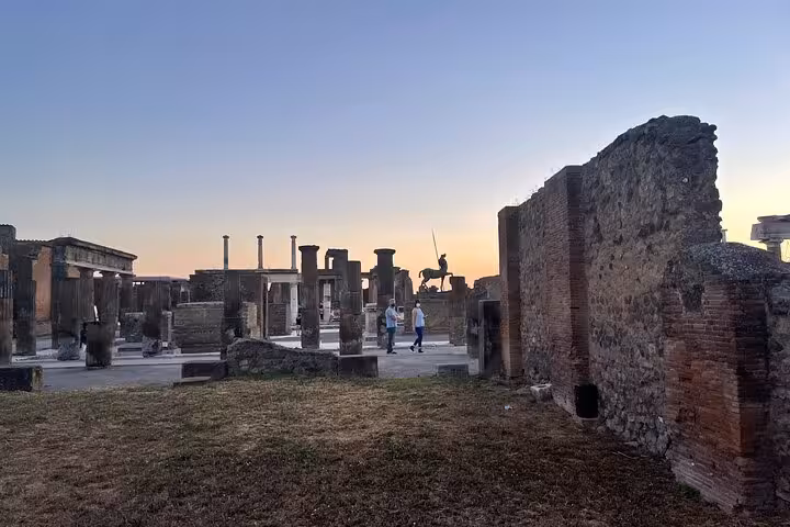 Explore Pompeii's ancient ruins at sunset, showcasing historic columns and statues under a colorful evening sky.