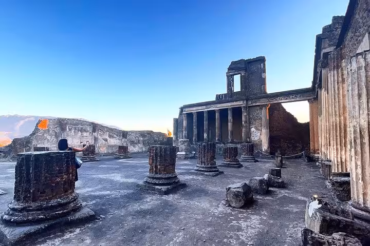 The majestic ruins of Pompeii's ancient architecture stand against a stunning sunset backdrop, inviting exploration.