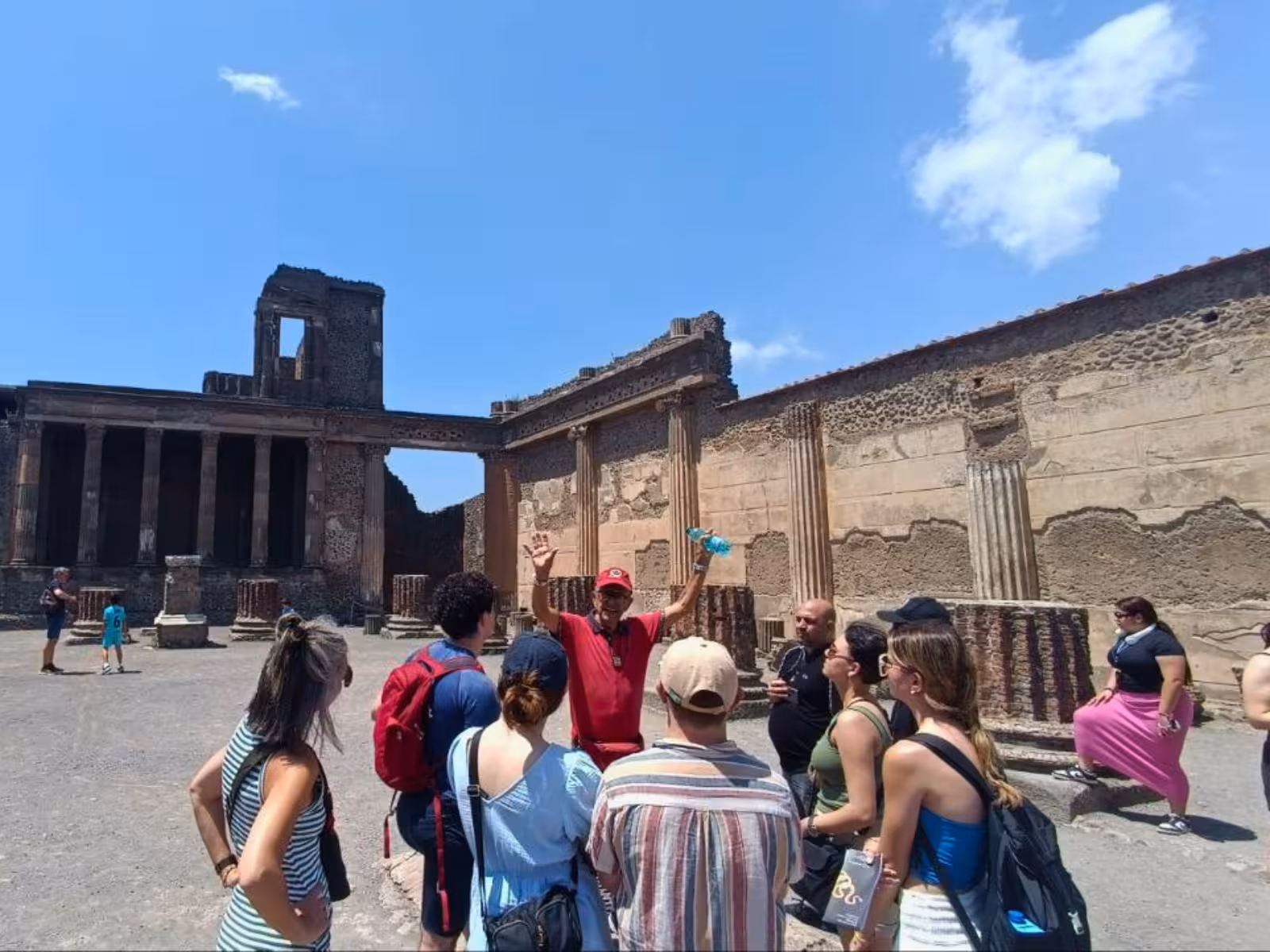 Tour group exploring ancient ruins of Pompeii with a guide under a clear blue sky.
