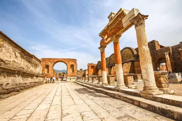 The ancient columns and arches of Pompeii's ruins stand under a clear sky on a walking tour.