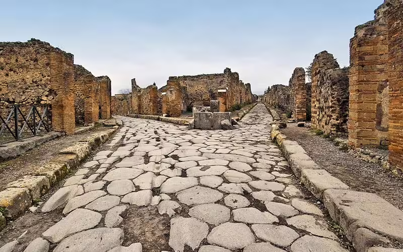 Ancient stone-paved street and ruined houses in Pompeii archaeological site on a guided daily walking tour from Naples