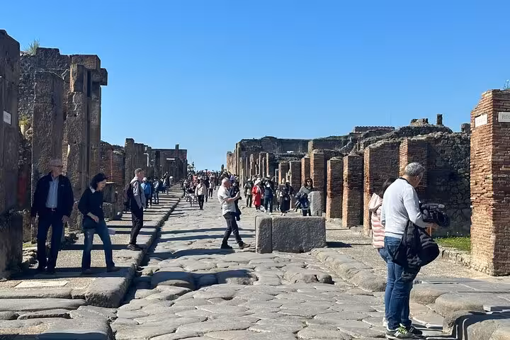 Visitors strolling along ancient stone streets in Pompeii, guided by an archaeologist during the tour.
