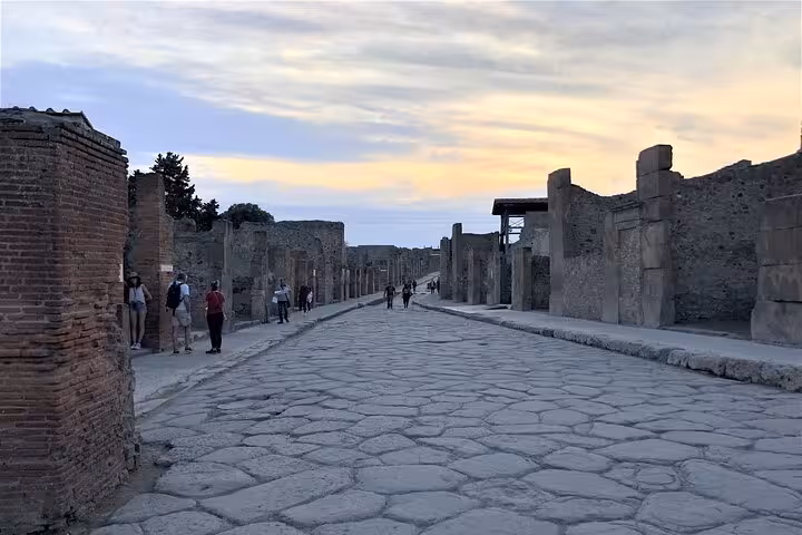Tourists explore the ancient stone streets of Pompeii at dusk, capturing the historic ambiance of the site.