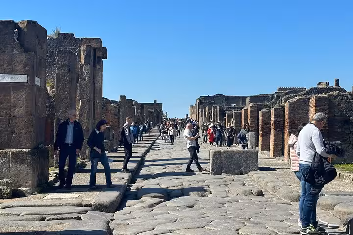 Visitors exploring the ancient stone streets of Pompeii under a clear blue sky on a guided tour from Amalfi Coast.