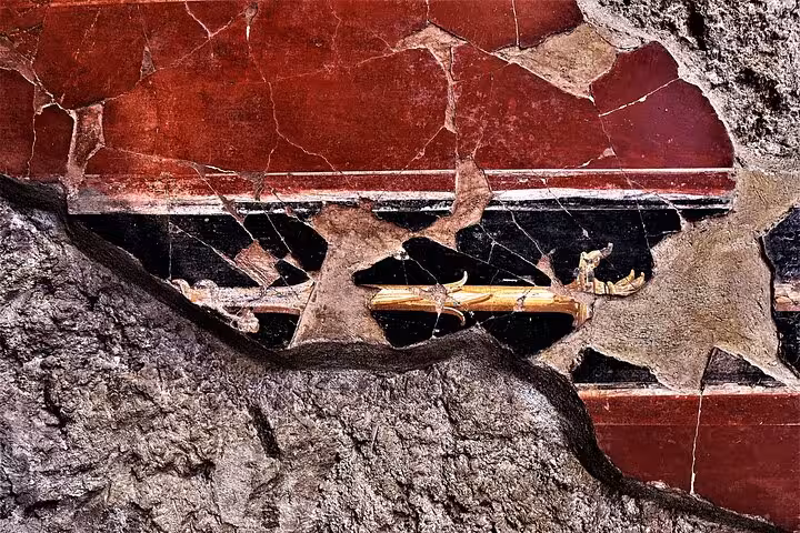 Detail of ancient Pompeii wall art with rich red and black hues, featured in a guided archaeological tour.
