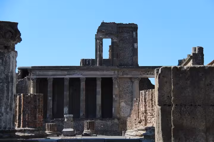 Ancient ruins of Pompeii's Basilica, featuring a grand colonnade under a clear blue sky, perfect for a historical tour.
