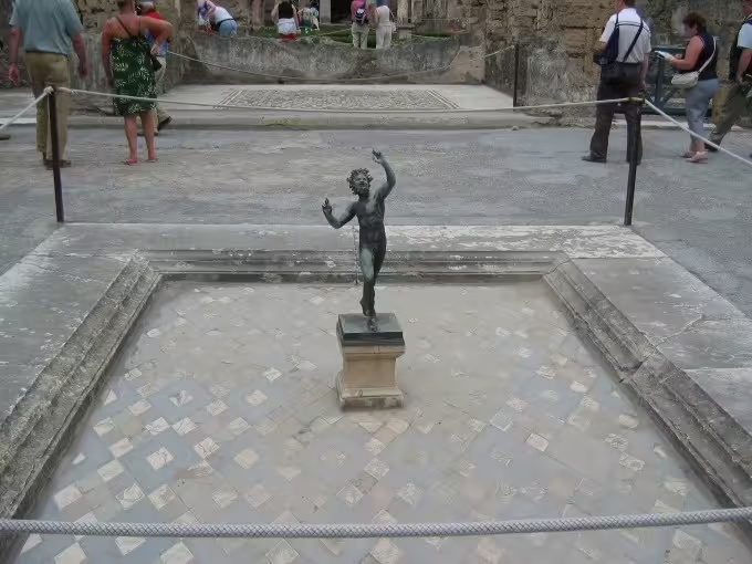 Bronze statue in Pompeii courtyard with mosaic floor, visitors on low cost Pompeii tour from Naples