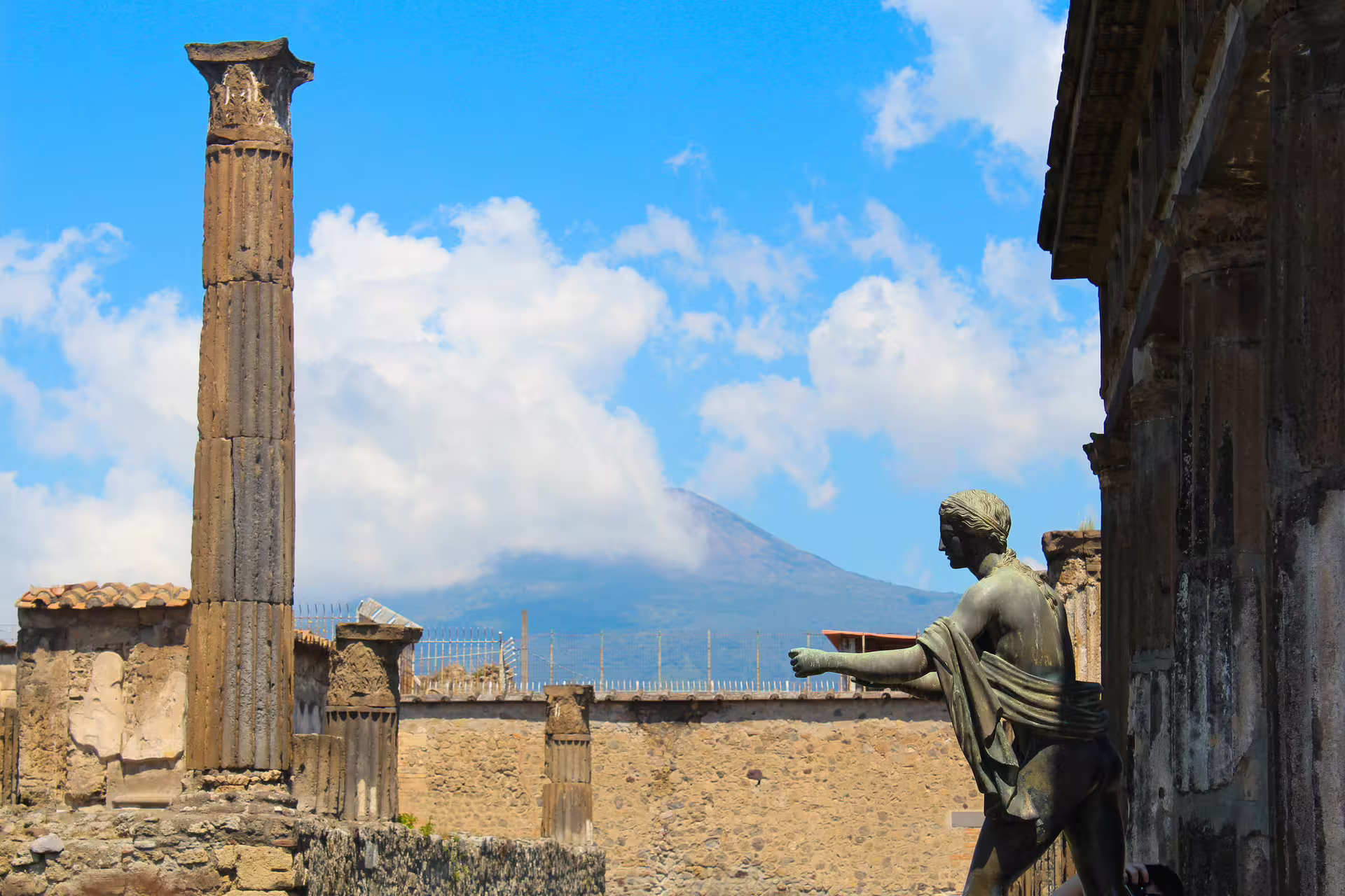Bronze statue and crumbling columns in Pompeii with Mount Vesuvius backdrop on a semi private afternoon tour from Rome