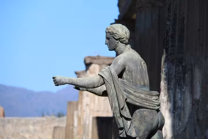 Close-up of a classical statue in Pompeii against a backdrop of ancient ruins and blue sky on a Rome to Pompeii tour.