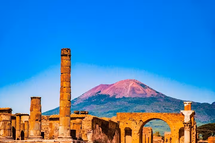 Explore the iconic columns and arches of Pompeii with a stunning view of Mount Vesuvius on a Naples port trip.