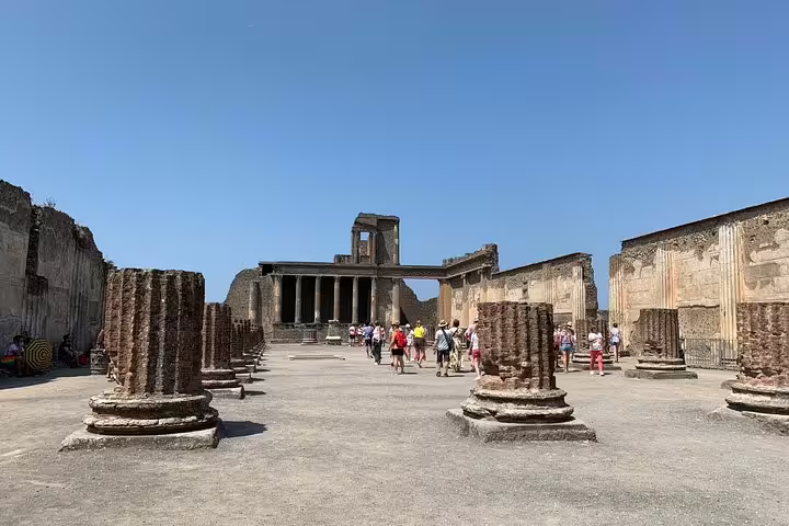 Tourists wander through the ancient ruins of Pompeii's Forum, surrounded by historic columns and architectural remnants.