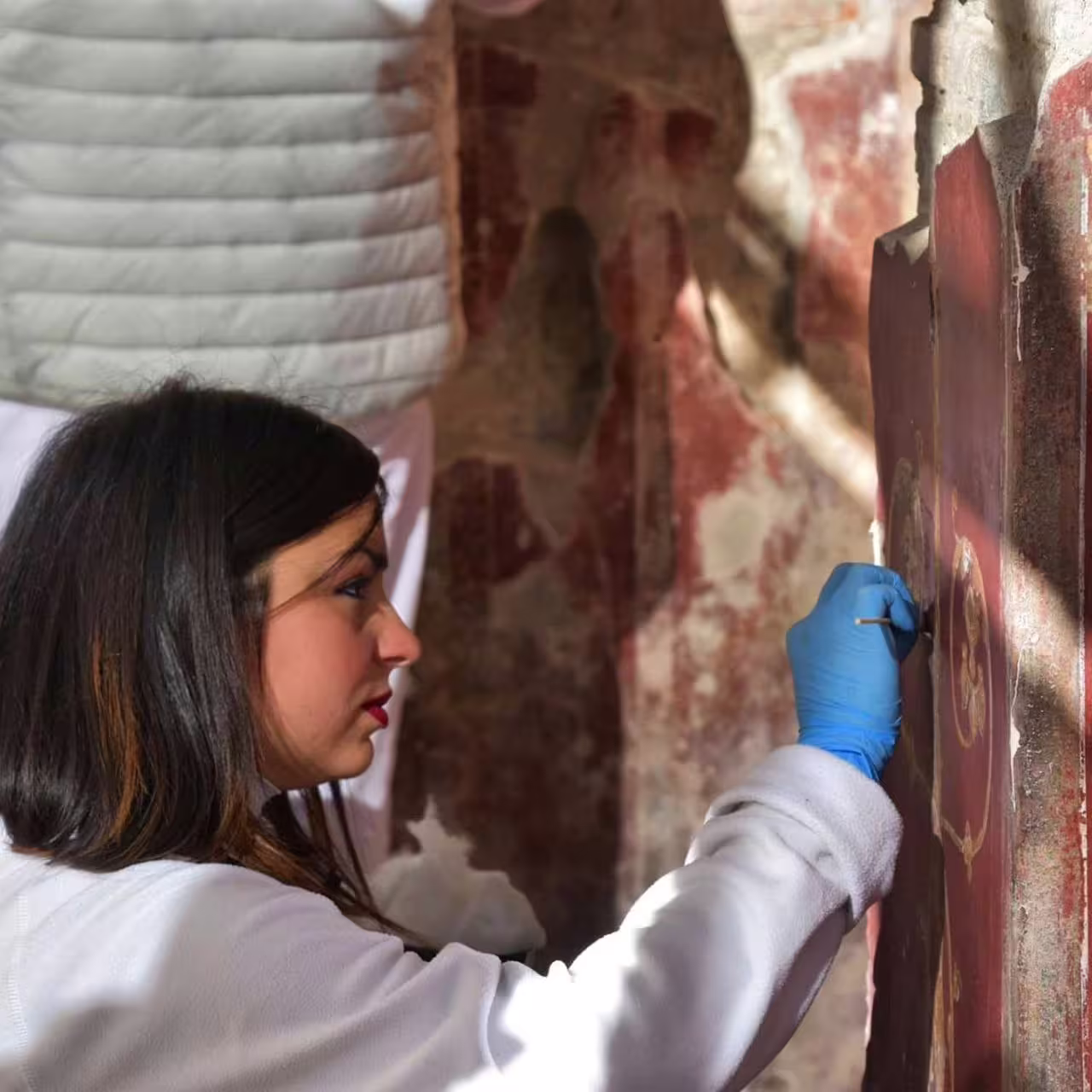 Restorer cleaning ancient Pompeii fresco during group tour from Naples, UNESCO ruins and history visit