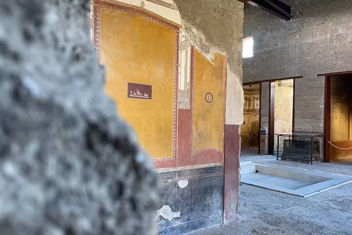 Interior view of a preserved Pompeii building featuring vibrant frescoes and ancient architecture, part of a guided tour experience.
