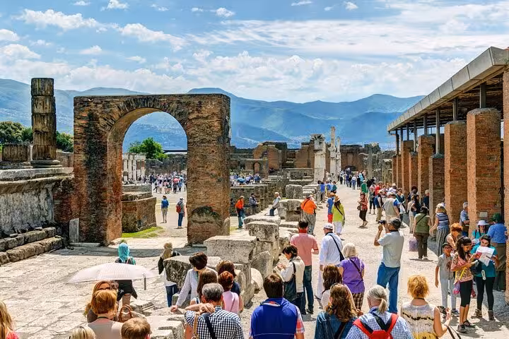 Visitors explore ancient ruins and arches on a guided tour of Pompeii with scenic mountain views.