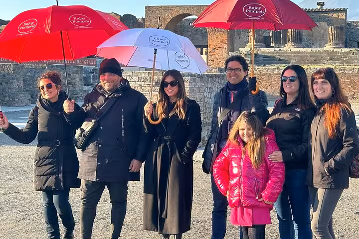 Group exploring Pompeii ruins with red umbrellas on guided tour from Positano, highlighting historical adventure.