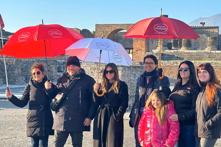 Tour group with umbrellas at Pompeii ruins, showcasing skip-the-line access and guided exploration from Naples.